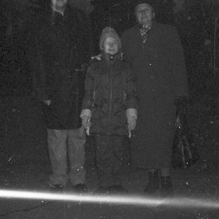 Here's a brief summary of the image: Two people stand on a ledge in low light.