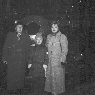 A family stands outdoors in winter clothing during snowfall.