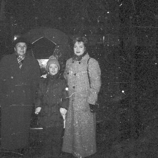 A family stands outdoors in winter clothing during snowfall.