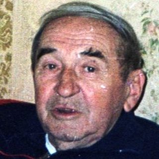 Man sits on a red couch in a patterned room.