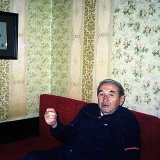Man sits on a red couch in a patterned room.
