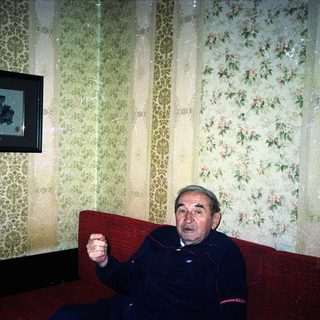 Man sits on a red couch in a patterned room.