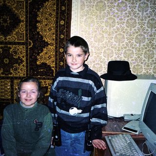 Two boys stand near a vintage computer with a rug.