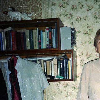 Woman stands in a room with books and clutter.