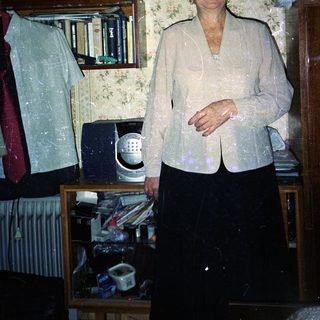 Woman stands in a room with books and clutter.