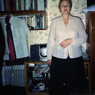 Woman stands in a room with books and clutter.