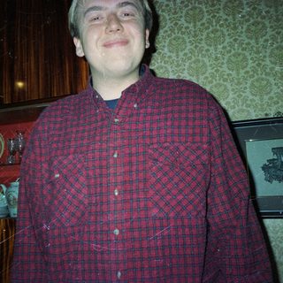 Man in plaid shirt stands in front of patterned wallpaper.