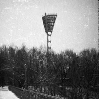 Snow-covered bridge leads towards a tall stadium light tower.