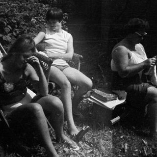 Here's a brief summary of the image: People relaxing outdoors, appearing to be in a wooded area.