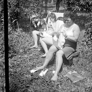 Here's a brief summary of the image: Two women and a baby relaxing outdoors in a grassy area.