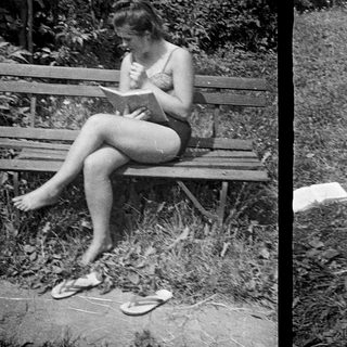Here's a brief summary of the image: Two girls reading outdoors on a bench and chair.