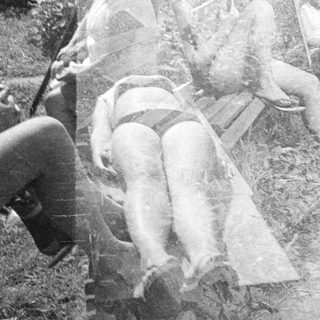Here's a brief summary of the image: Two women seated on a wooden bench; another reclined nearby.