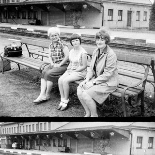 Three women sit on a bench near a train station.