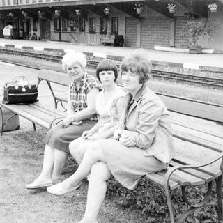 Three women sit on a bench near a train station.