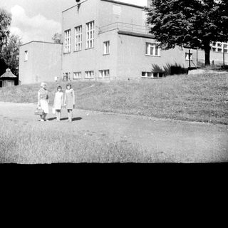 Here's a brief summary of the image: Two girls stand near a building, likely a school.