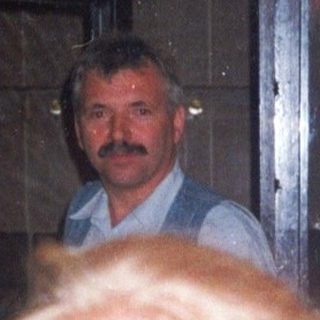 Woman stands in doorway with man visible behind her.