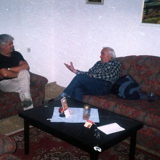 Two men seated on a patterned couch in a room.