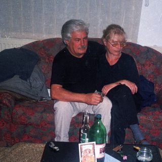 Two men seated on a sofa with a cluttered table.