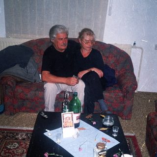 Two men seated on a sofa with a cluttered table.