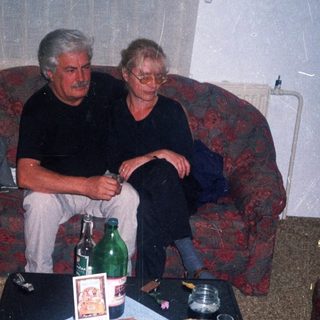 Two men seated on a sofa with a cluttered table.