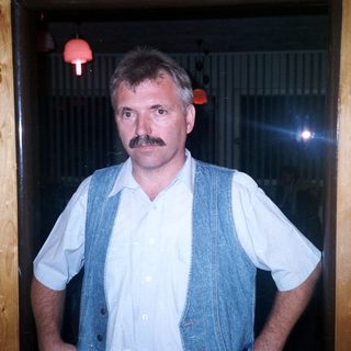 Man with mustache stands in a wooden-paneled room.