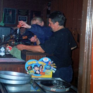 Person tending bar with customers in a dimly lit room.