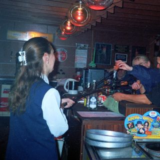 Person tending bar with customers in a dimly lit room.