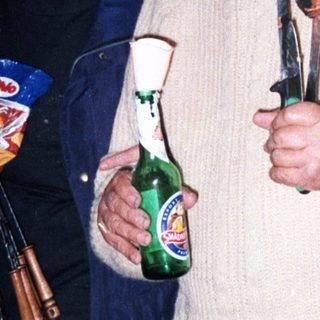 Two men on stairs holding food, drinks, and a knife.