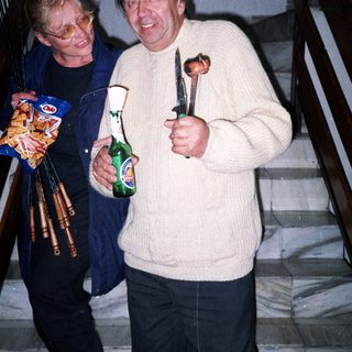 Two men on stairs holding food, drinks, and a knife.