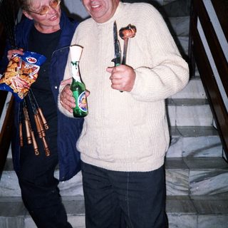 Two men on stairs holding food, drinks, and a knife.