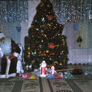 Two Santa Clauses stand near a decorated Christmas tree.