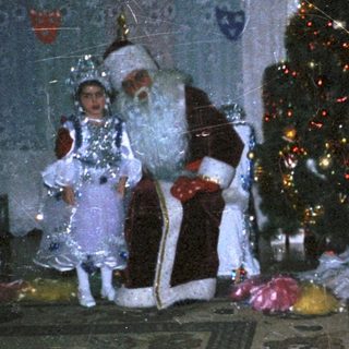 Two Santa Clauses stand near a decorated Christmas tree.