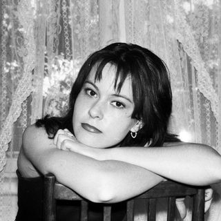 Here's a brief summary: Woman with short hair sits behind a chair.