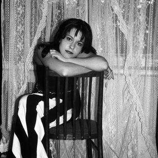 Here's a brief summary of the image: Woman seated on a chair, posing for a black and white portrait.