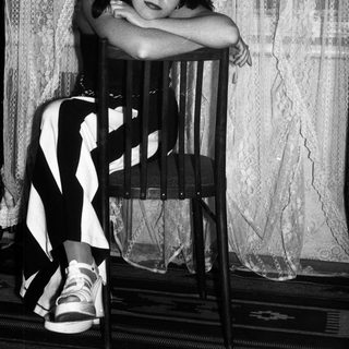 Here's a brief summary of the image: Woman seated on a chair, posing for a black and white portrait.