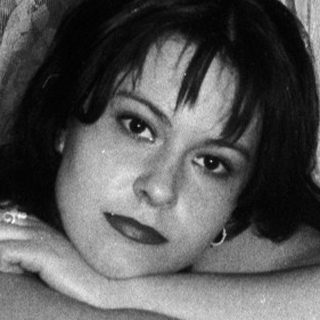 Here's a brief summary of the image: Woman seated on a chair, posing for a black and white portrait.