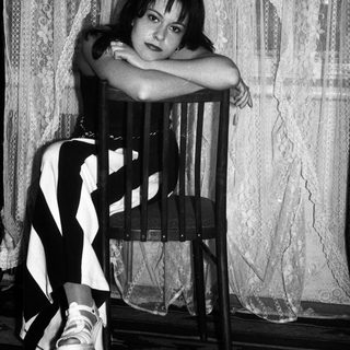 Here's a brief summary of the image: Woman seated on a chair, posing for a black and white portrait.