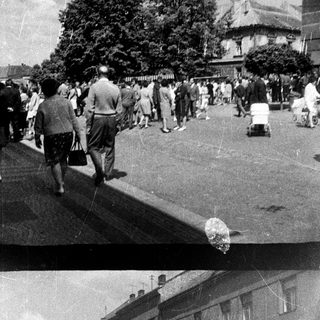 Black and white photo depicts people walking down a street.