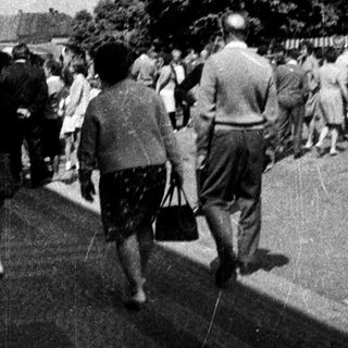 Black and white photo depicts people walking down a street.