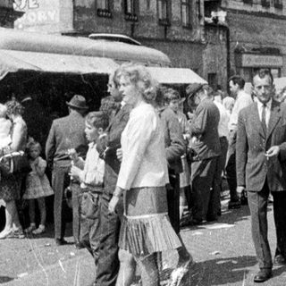 Crowded town square scene, people socializing and passing by.