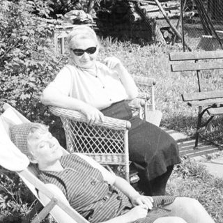 Here's a brief summary of the image: Two people relax in chairs, a man sits on a bench.