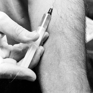 Here's a brief summary of the image: Syringe poised to inject fluid into a person's arm.