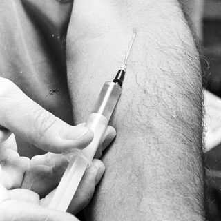 Here's a brief summary of the image: Syringe poised to inject fluid into a person's arm.