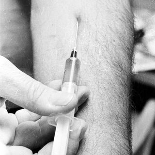 Here's a brief summary of the image: Syringe injecting fluid into a person's arm.