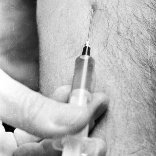 Here's a brief summary of the image: Needle being prepared for injection into an arm.