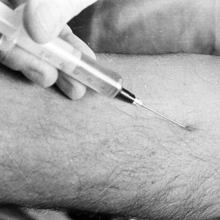 Here's a brief summary of the image: Needle being inserted into an arm for injection.