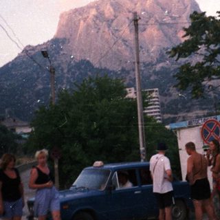 Group of people near a taxi in front of a mountain.