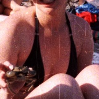 Crowded beach scene with a woman relaxing on a blanket.