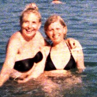 Two girls swim in ocean with other people present.