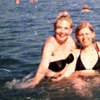 Two girls swim in ocean with other people present.